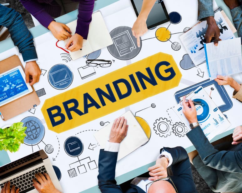Un groupe de personnes collabore autour d'une table recouverte de papiers, de graphiques et du mot « Branding » affiché bien en évidence au centre.