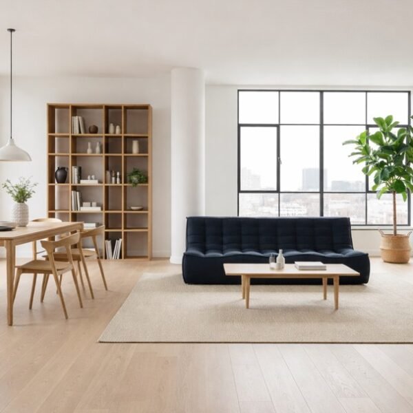 Salon et salle à manger modernes avec de grandes fenêtres, des meubles en bois clair, un canapé foncé, une table à manger avec des chaises, une étagère, une plante en pot et un décor minimaliste.