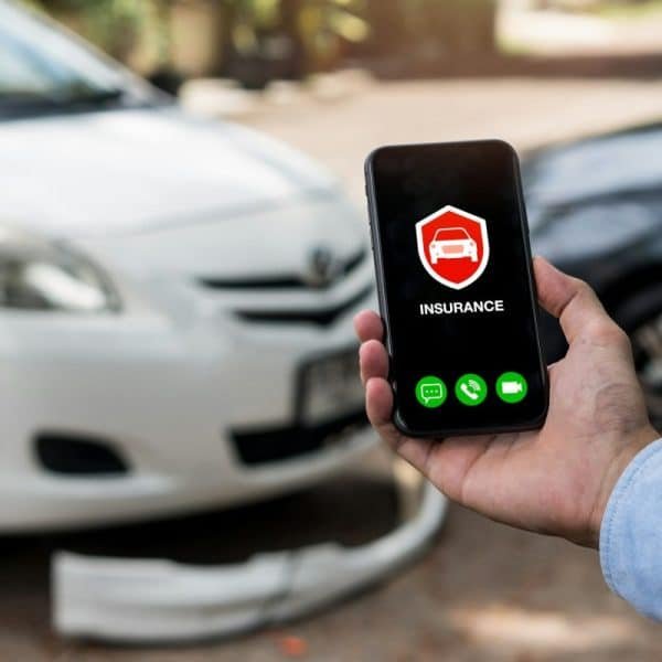 Concept d'assurance automobile : un homme utilise son téléphone pour appeler un agent d'assurance après un accident de voiture.