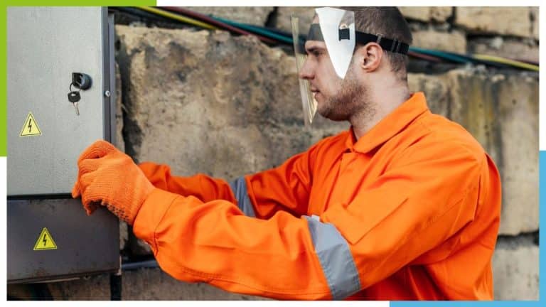 Une personne portant un uniforme de sécurité orange et des gants travaille sur un panneau électrique à l’extérieur.