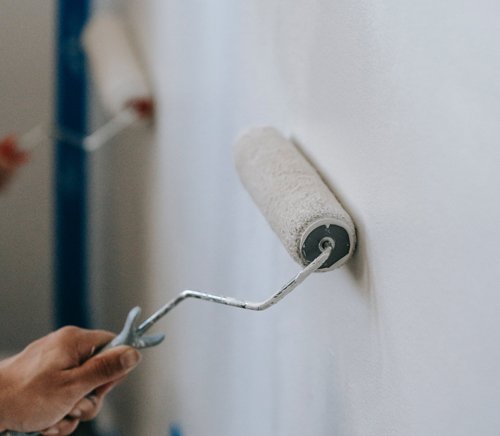 Gros plan d'une personne utilisant un rouleau de peinture pour appliquer de la peinture blanche sur un mur.