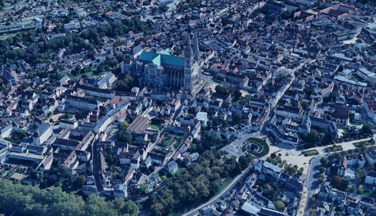 Vue aérienne de Chartres historique avec une cathédrale proéminente au centre, entourée de bâtiments denses et de rues bordées d'arbres.
