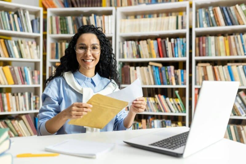 Cheerful librarian organizing files at laptop in library