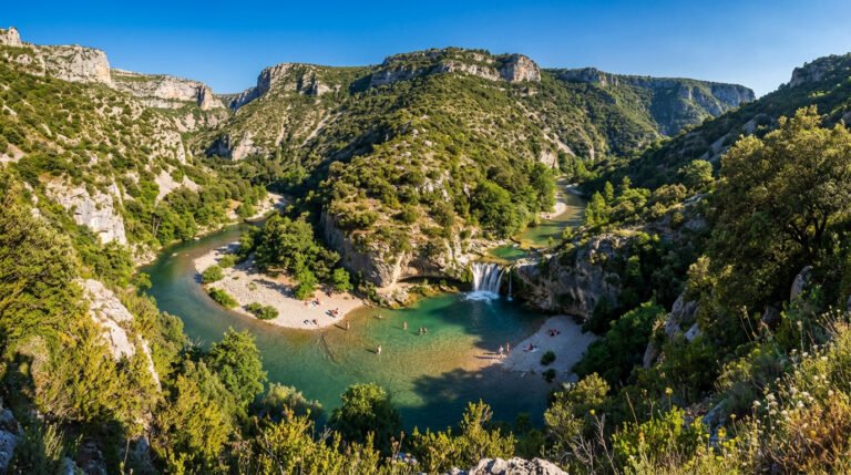 Vue aérienne d'un canyon verdoyant avec une rivière turquoise, une cascade et des baigneurs sur les plages ensoleillées.