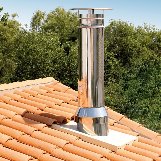 Un tuyau de cheminée en métal brillant est installé sur un toit recouvert de tuiles en céramique orange, avec des arbres verts en arrière plan.