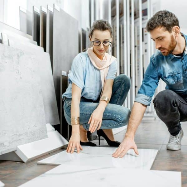 Deux personnes choisissent des carreaux dans une salle d'exposition et examinent les motifs marbrés sur le sol. Ils sont accroupis et concentrés sur les échantillons de carreaux.