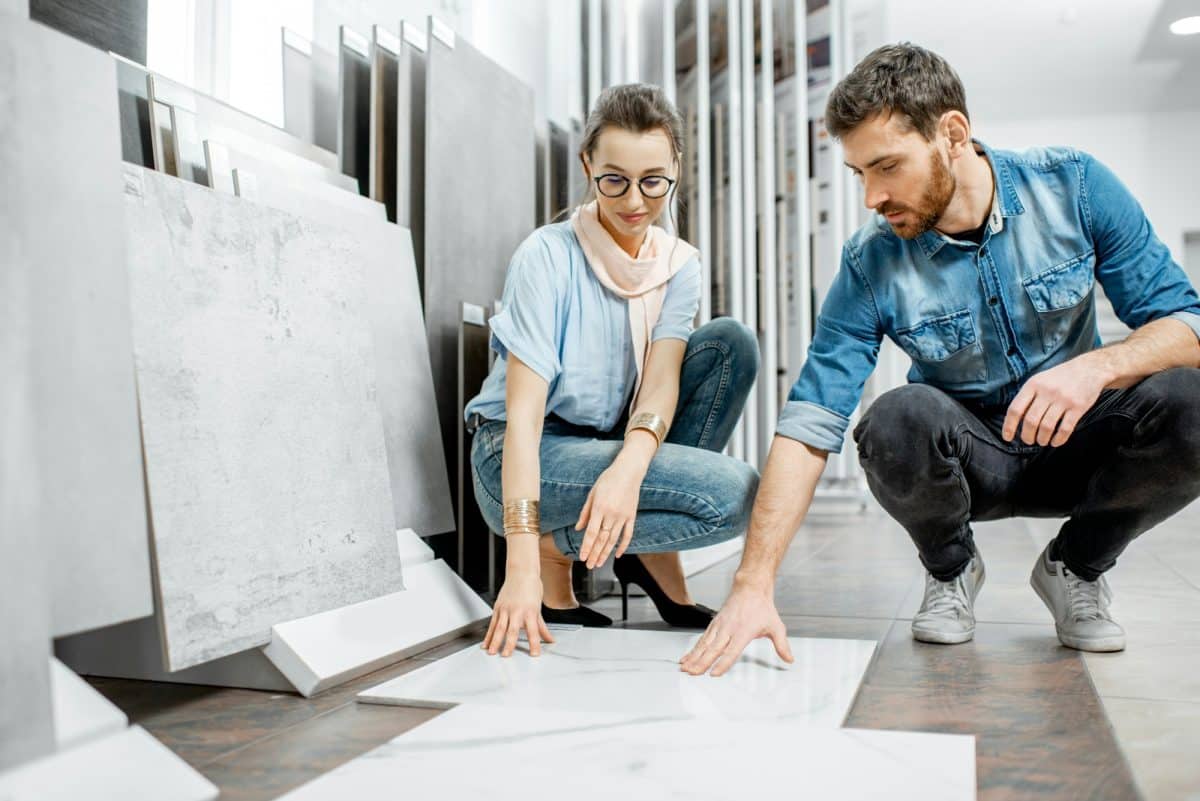 Deux personnes choisissent des carreaux dans une salle d'exposition et examinent les motifs marbrés sur le sol. Ils sont accroupis et concentrés sur les échantillons de carreaux.