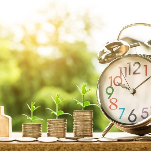Un réveil avec des pièces de monnaie et une maison en arrière plan.