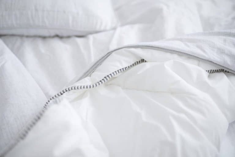 Gros plan d'un lit blanc avec une couette moelleuse à bordure rayée, repliée sur elle même. Des oreillers blancs en arrière plan.