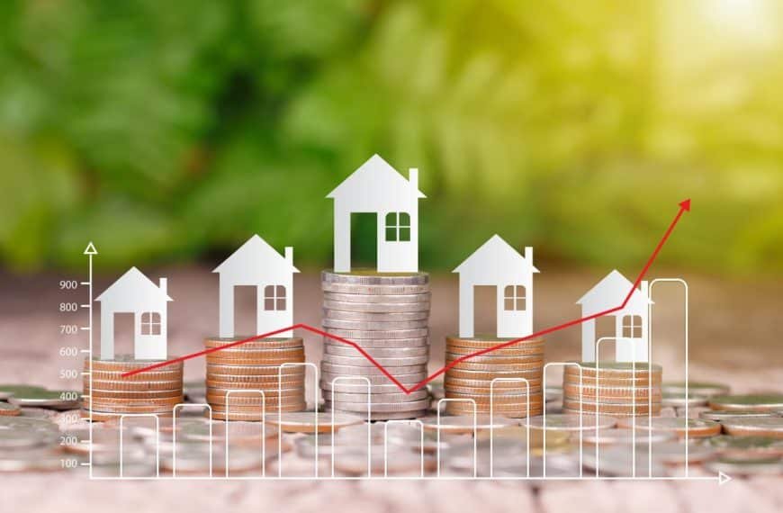 Des piles de pièces avec des icônes de maison sur le dessus, superposées à un graphique en ligne rouge, symbolisant les tendances du marché immobilier sur un fond vert flou.