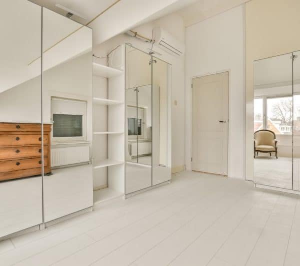 Une chambre blanche avec des miroirs et une commode.