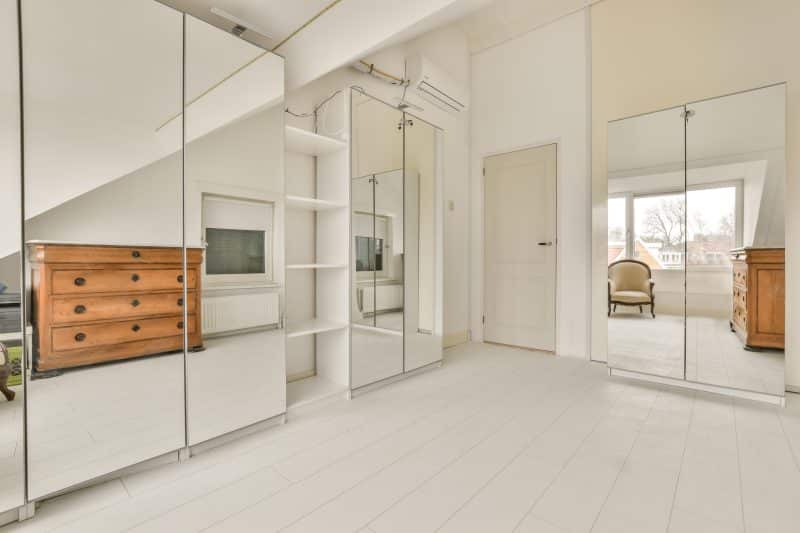 Une chambre blanche avec des miroirs et une commode.