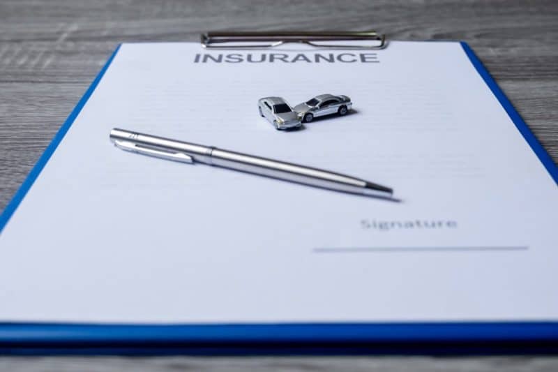 Un stylo, deux petites voitures et un presse papiers avec un document d'assurance sont disposés sur une surface en bois. Un stylo, deux petites voitures et un presse papiers avec un document d'assurance sont disposés sur une surface en bois.