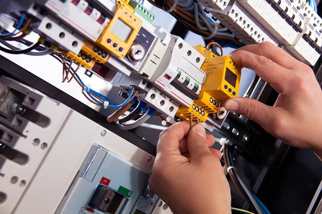Mains installant un composant dans un panneau de disjoncteurs électriques, entouré de câblage et de disjoncteurs modulaires.