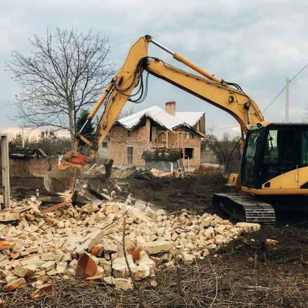 Excavator destroying brick house on land in countryside