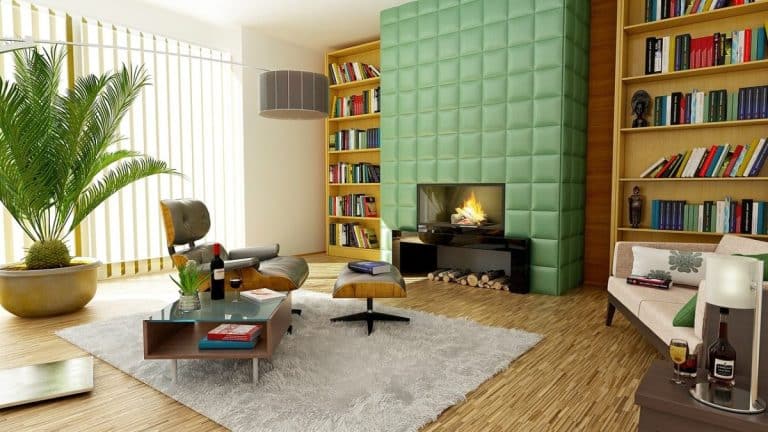 Salon moderne avec cheminée à panneaux verts, bibliothèques, fauteuils, canapé, table basse et grande plante en pot. La lumière naturelle entre par des stores verticaux.