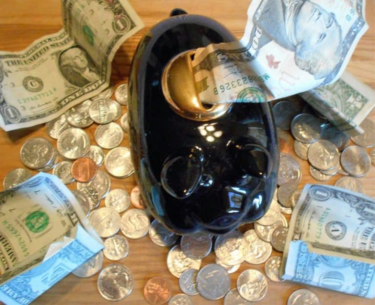 Une tirelire noire entourée de pièces de monnaie assorties et de diverses dénominations de billets de dollars américains sur une surface en bois.