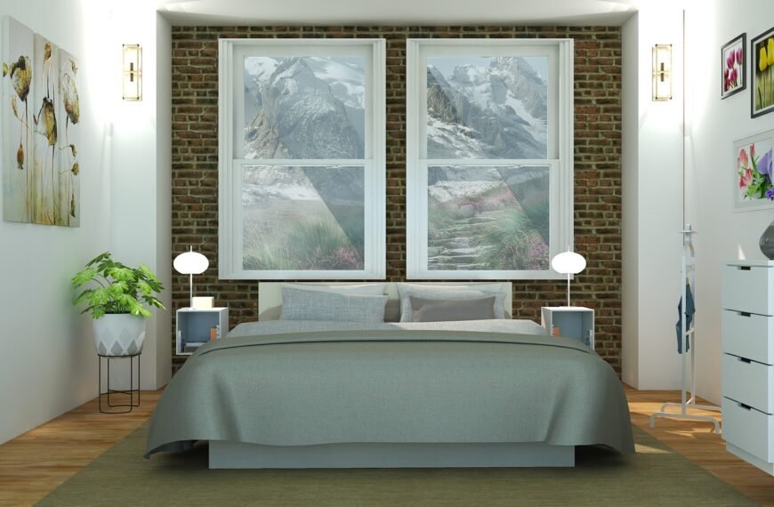 Une chambre moderne avec un lit gris, des tables de chevet équipées de lampes, un mur d'accent en briques et deux fenêtres donnant sur un paysage de montagne. Des œuvres d'art, des plantes et des commodes agrémentent la pièce.