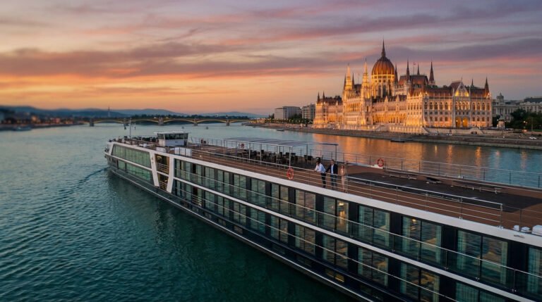 Modern river cruise ship on Danube at golden hour, Budapest Parliament illuminated. Passengers enjoy panoramic city views.