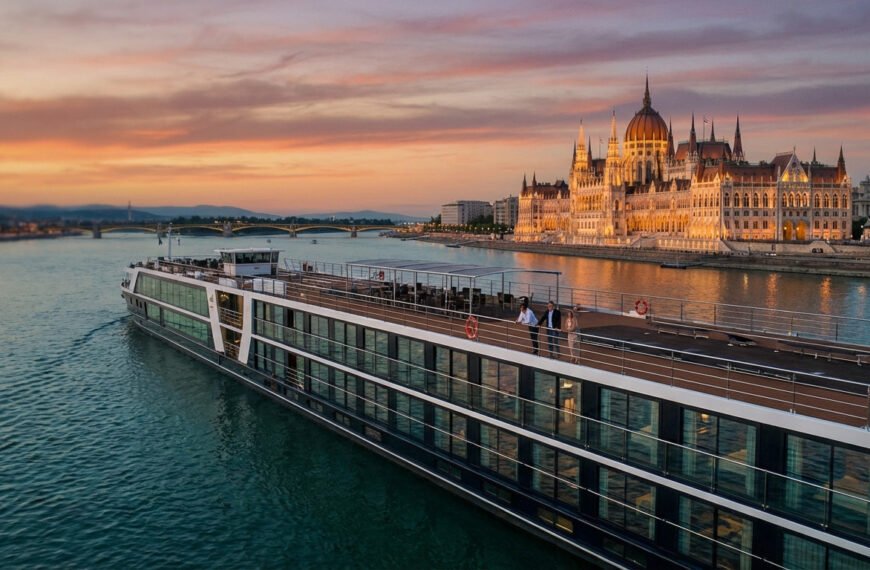 Modern river cruise ship on Danube at golden hour, Budapest Parliament illuminated. Passengers enjoy panoramic city views.