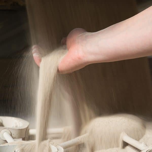 Une main tient et laisse couler du sable fin dans un récipient rempli de sable.