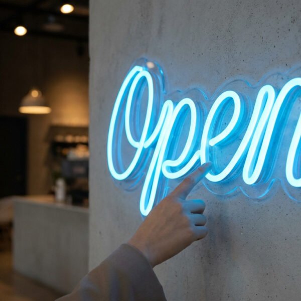 Une personne pointe du doigt un néon bleu "Ouvert" fixé sur un mur à l'intérieur d'un café moderne faiblement éclairé.
