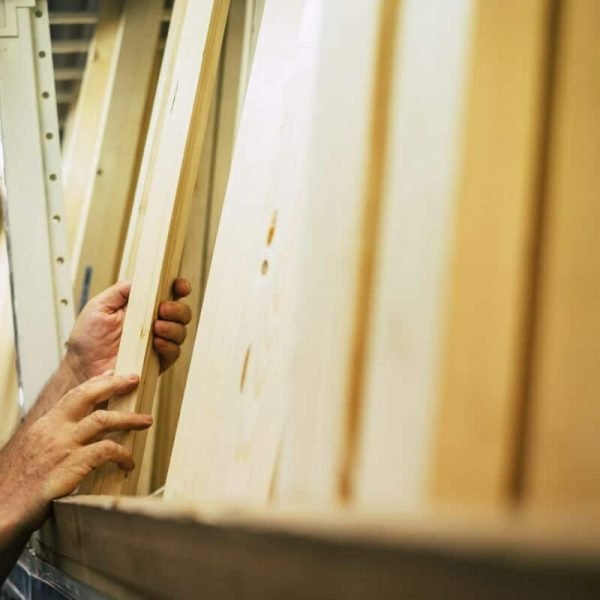 Mains sélectionnant des planches de bois sur une étagère dans une quincaillerie.