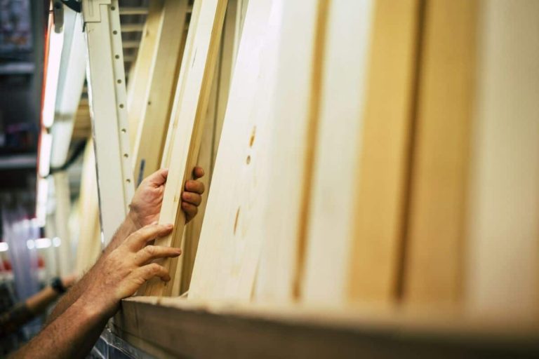 Mains sélectionnant des planches de bois sur une étagère dans une quincaillerie.