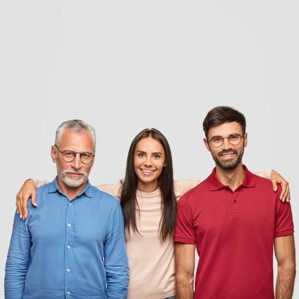 Trois personnes se tiennent côte à côte sur un fond uni, la femme au centre souriant et entourant de ses bras les deux hommes de part et d'autre.
