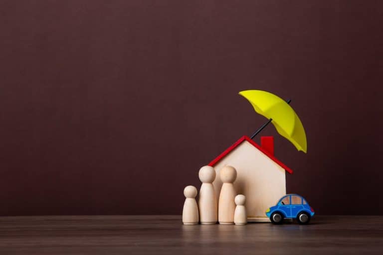 Quatre figurines en bois, une maison de jouets et une petite voiture bleue se tiennent sous un parapluie jaune, symbolisant la protection de la famille, de la maison et du véhicule.