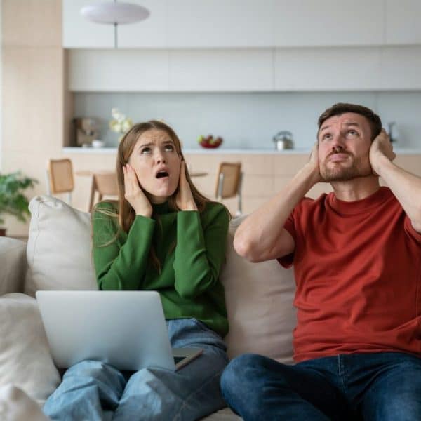 Husband and wife covered ears in anger due to loud noise of housemates. Life multi-storey building.