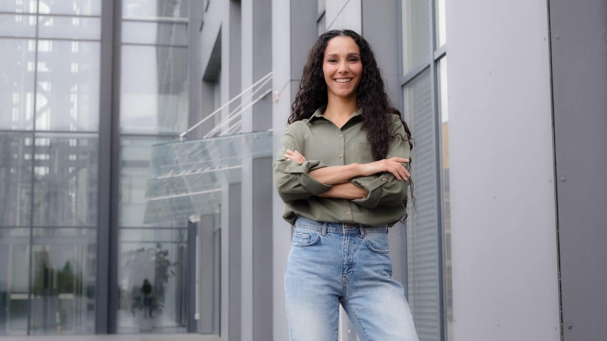 In city downtown background standing single smiling happy proud 30s woman in casual blouse strong