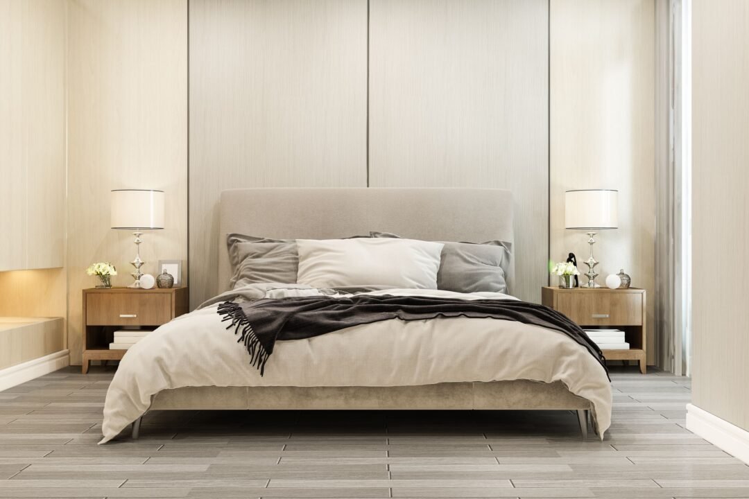 Chambre à coucher moderne avec un grand lit, une literie neutre, deux tables de nuit en bois, des lampes de table et des objets de décoration sur des murs et un sol de couleur claire.