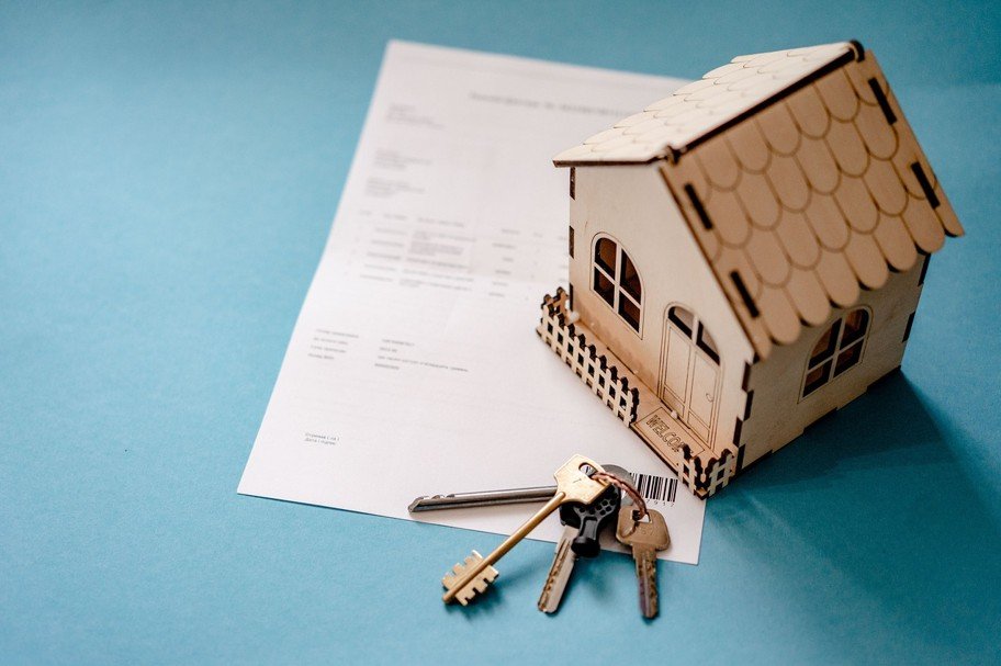 Une petite maquette de maison et un trousseau de clés reposent sur un document contenant du texte, le tout placé sur une surface bleu clair.