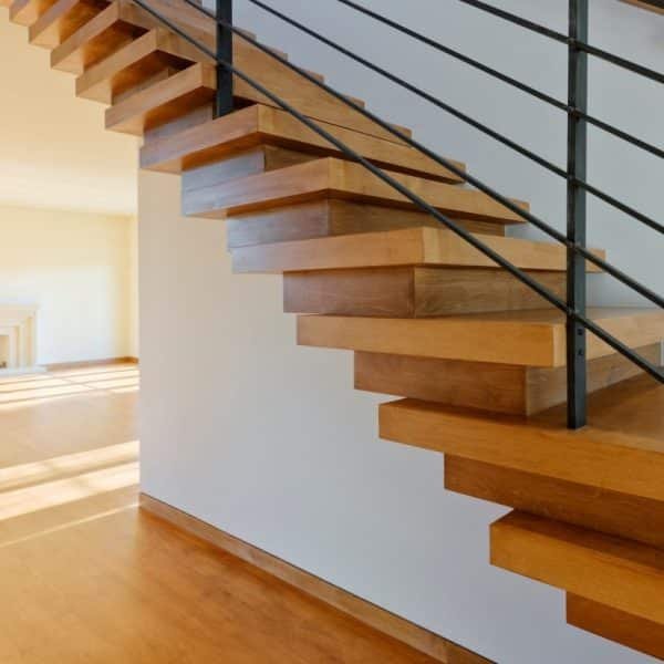 Escalier flottant en bois avec rampe en métal noir, menant à un étage supérieur. La lumière du soleil filtre dans la pièce, mettant en valeur les lignes épurées et le design minimaliste. Une cheminée est visible à proximité.