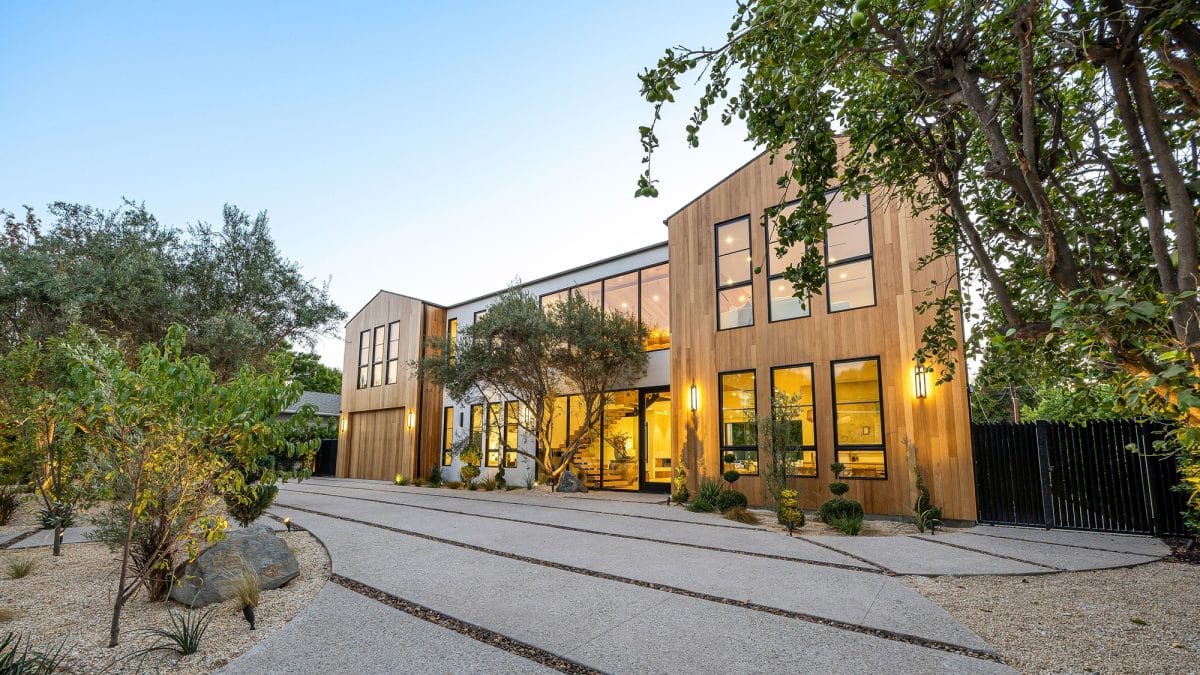 Modern wooden house with large windows and trees.