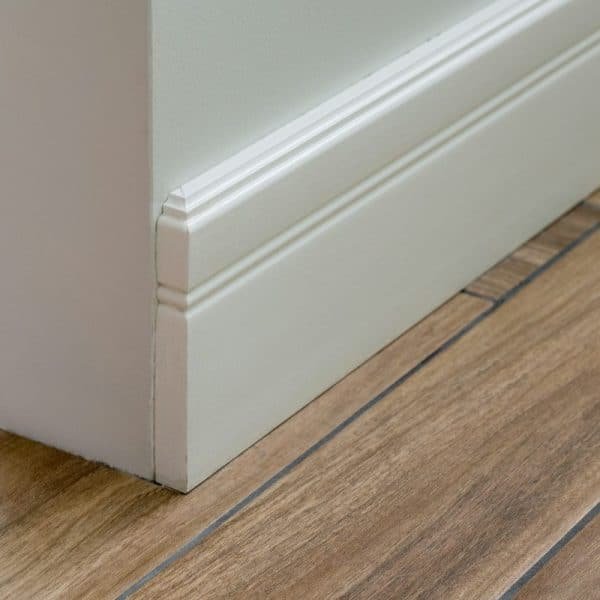 Gros plan d'une plinthe blanche et d'un coin d'un mur avec un parquet à motifs en bois.