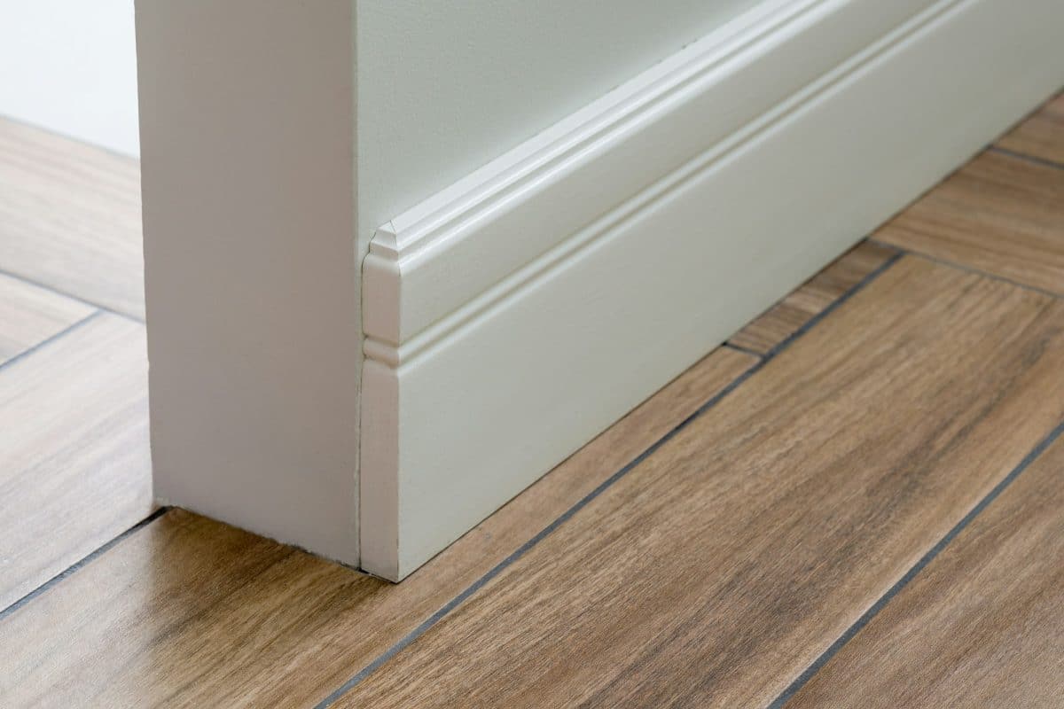 Gros plan d'une plinthe blanche et d'un coin d'un mur avec un parquet à motifs en bois.