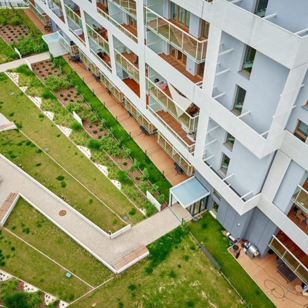Vue aérienne d'un immeuble d'appartements moderne avec terrasses et cour paysagée comportant des allées et des espaces verts.