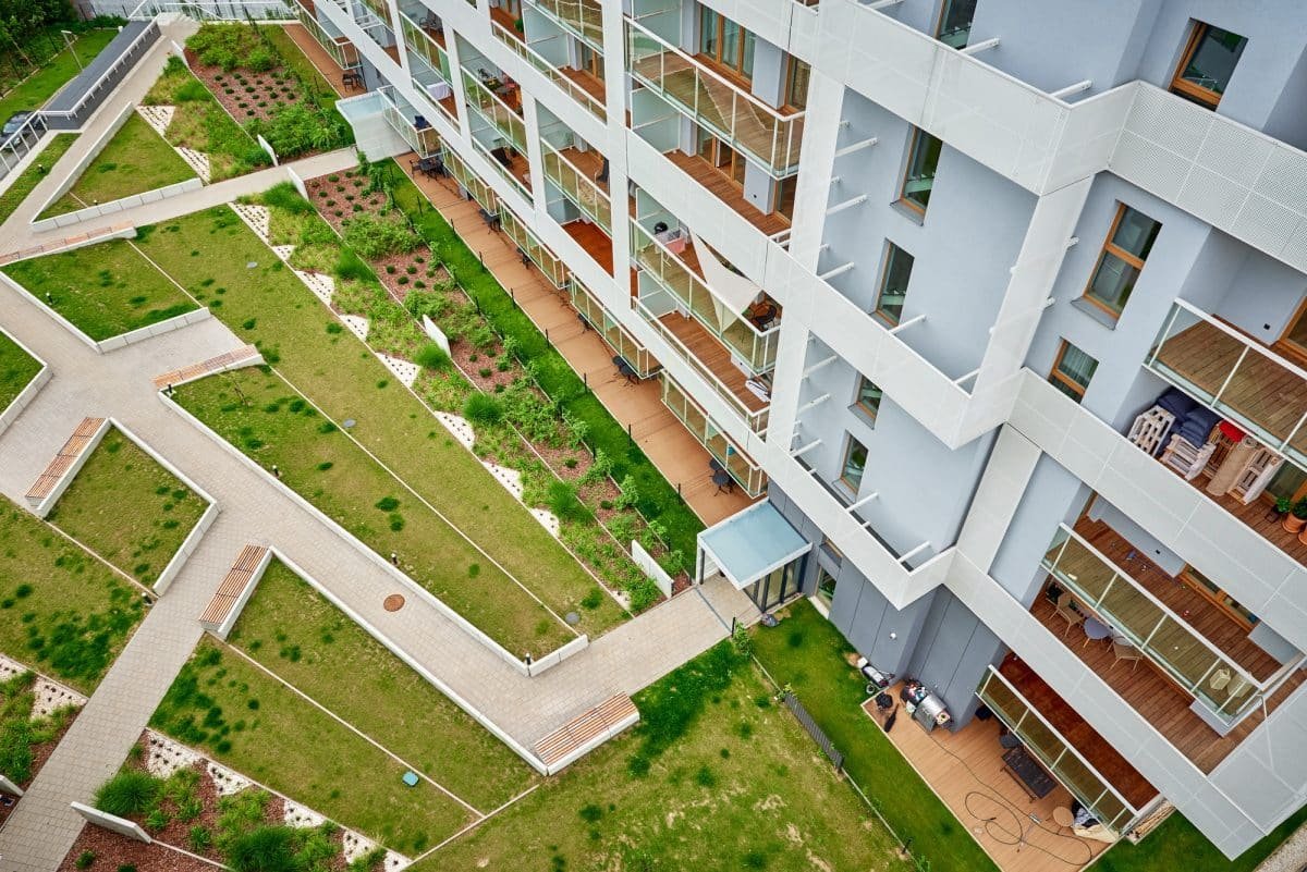 Vue aérienne d'un immeuble d'appartements moderne avec terrasses et cour paysagée comportant des allées et des espaces verts.