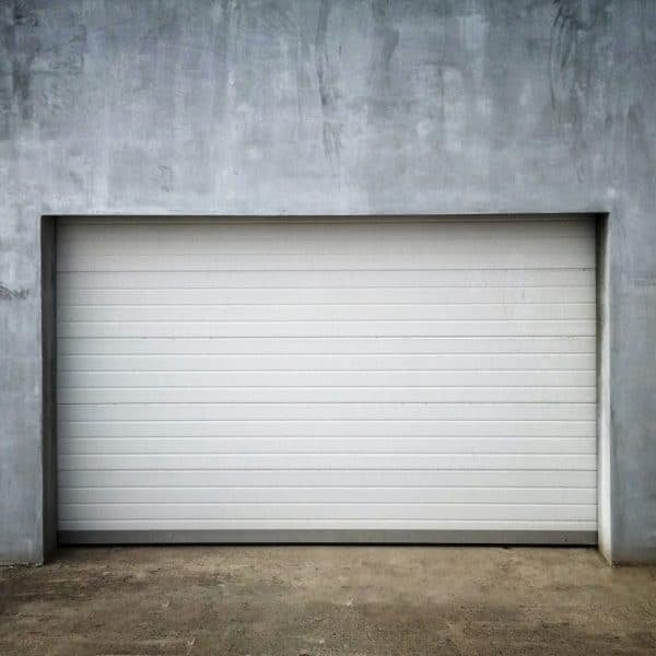 Une porte de garage fermée, blanche et moderne est encastrée dans un mur de béton lisse et gris.