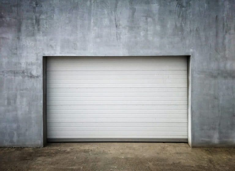 Une porte de garage fermée, blanche et moderne est encastrée dans un mur de béton lisse et gris.