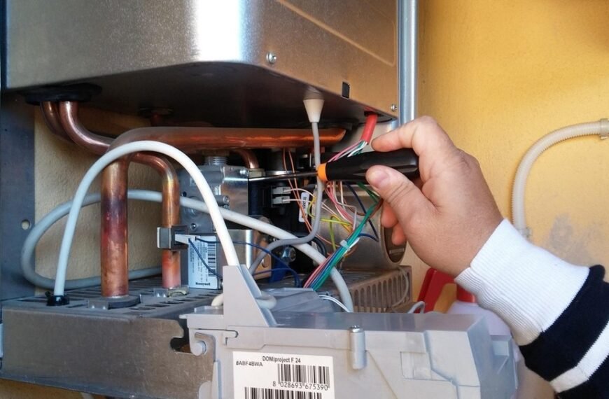 Une personne utilise un tournevis pour travailler sur le câblage électrique à l'intérieur d'un appareil métallique ouvert monté sur un mur.