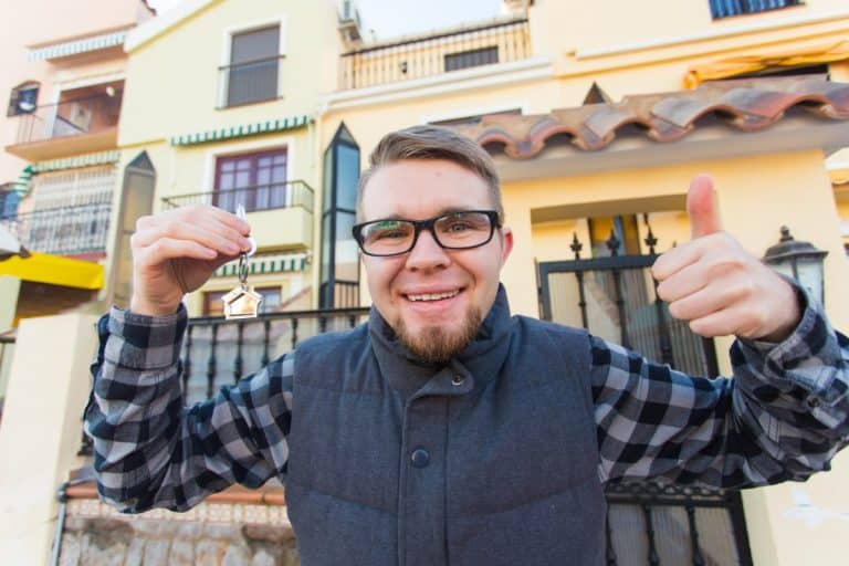 Ownership, real estate, property and tenant concept - Portrait of a cheerful young man holding key