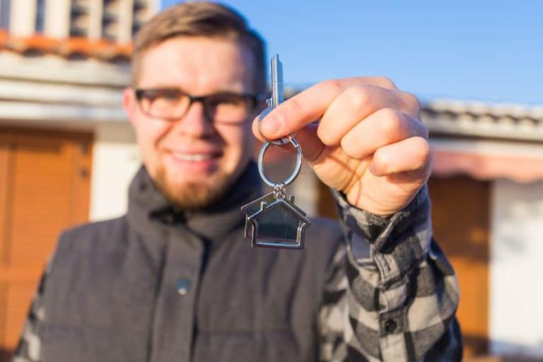 Un homme tenant une clé de maison devant une maison.