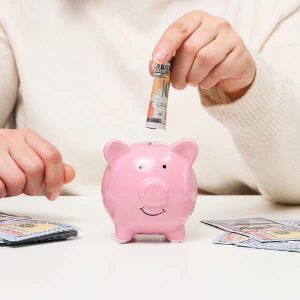 Une personne place un billet dans une tirelire pour économiser