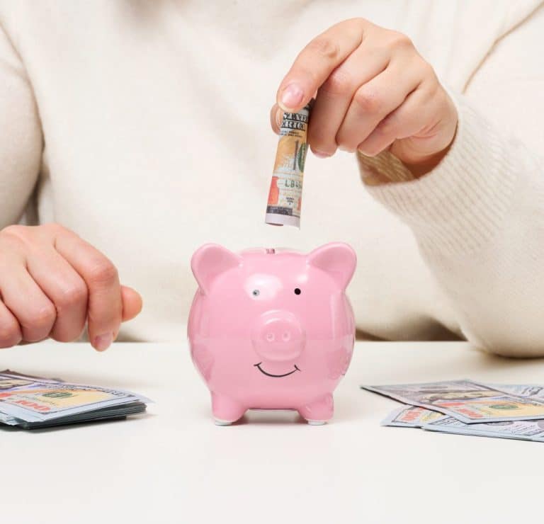 Une personne place un billet dans une tirelire pour économiser