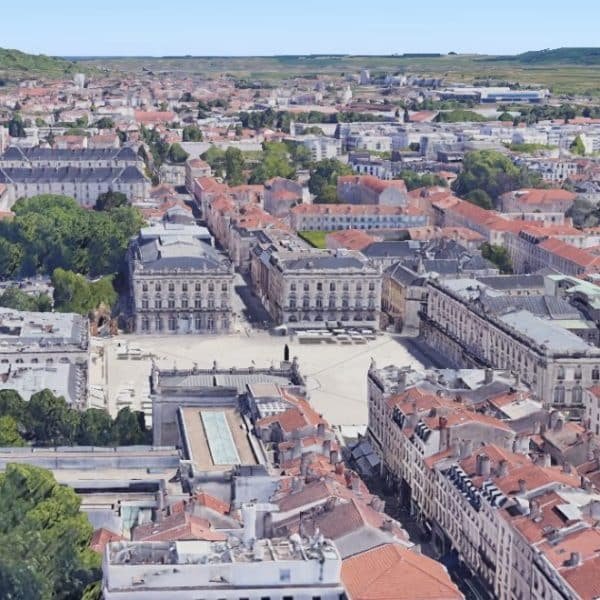 Vue aérienne d'un paysage urbain européen avec des bâtiments aux toits rouges, une place centrale et de la verdure environnante.