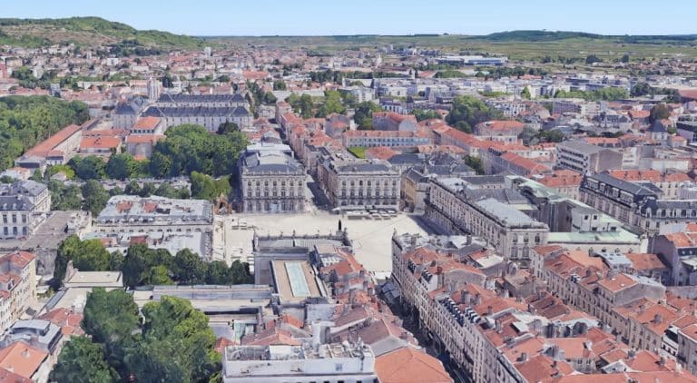 Vue aérienne d'un paysage urbain européen avec des bâtiments aux toits rouges, une place centrale et de la verdure environnante.