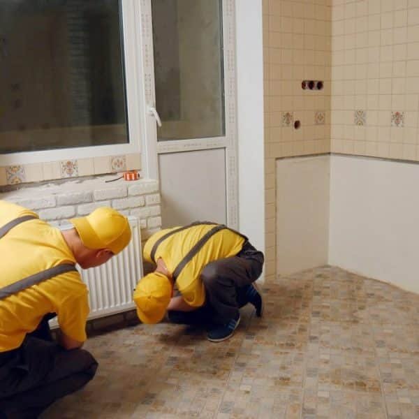 Deux ouvriers en uniformes jaunes installent des panneaux de briques blanches sur un mur d'une pièce carrelée.